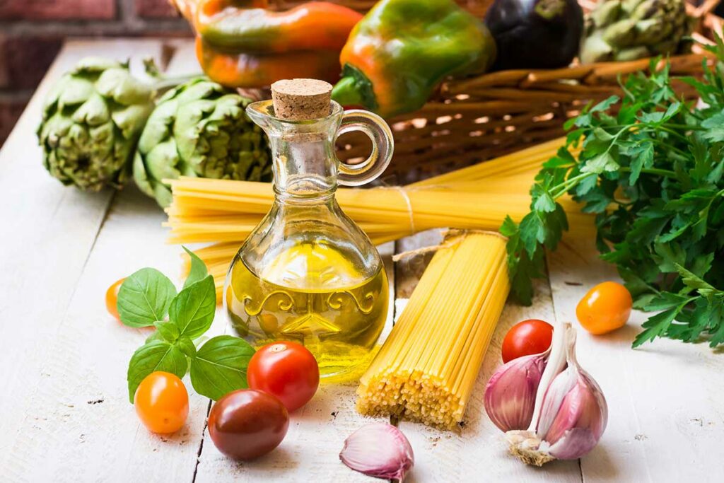 Menu tipico della dieta mediterranea con in primo piano spaghetti, olio, pomodori e verdure