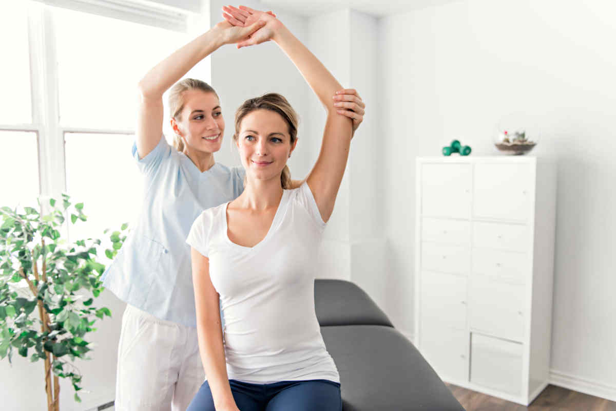 ragazza che effettua una ginnastica curativa in uno studio di fisioterapia con dottoressa giovane che le alza il braccio