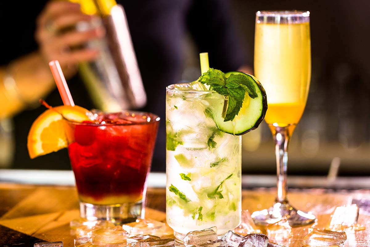 Bancone del bar con sopra dei cocktail colorati e un calice di vino bianco