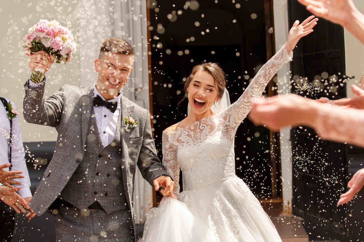 coppia di sposi felice e sorridente mentre gli lanciano il riso addosso per festeggiare