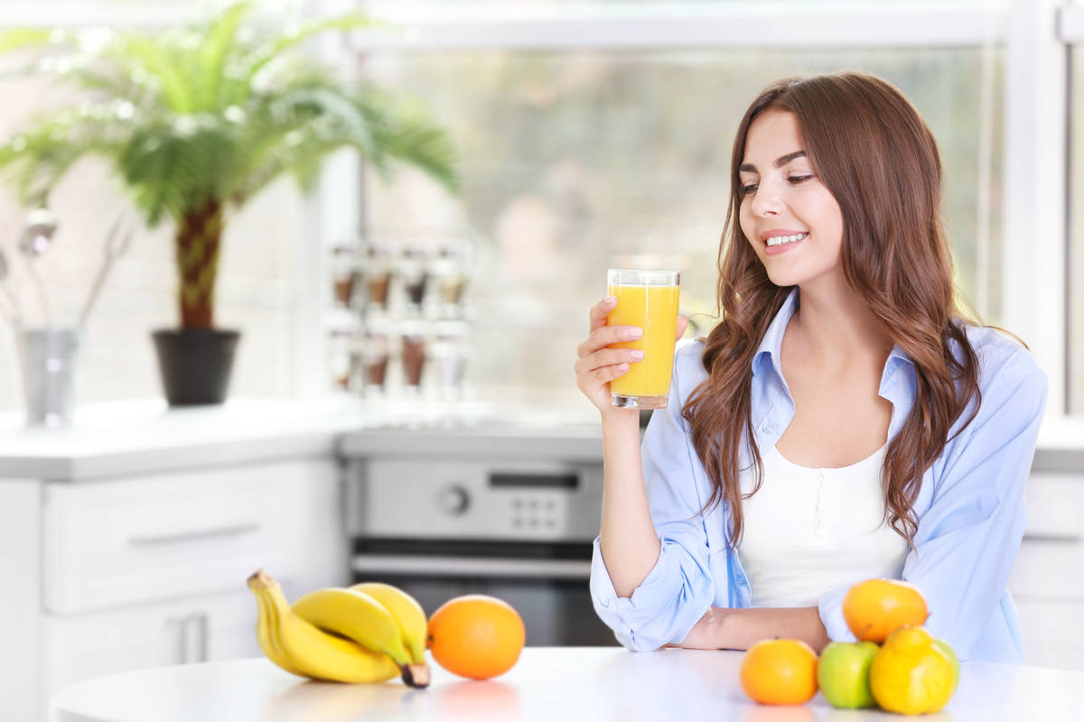 ragazza seduta in cucina, beve spremuta di arancia