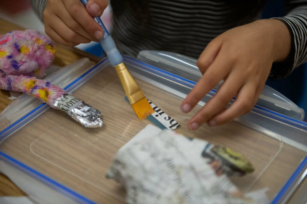 mani di bambina che lavorano con un pennello la carta di giornale, poggiata su un tavolo