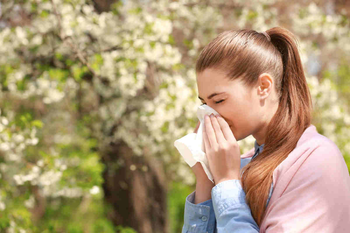ragazza che si soffia il naso presa da una crisi allergica tra i fiori e le piante