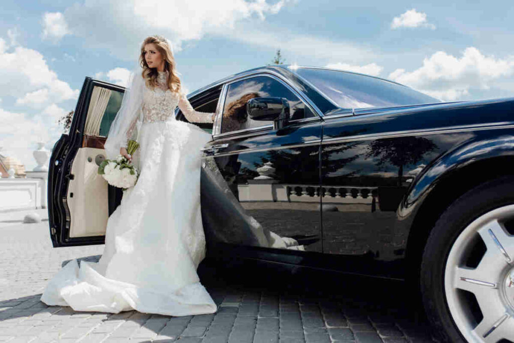 giovane donna sposa che sta uscendo da un auto di lusso di colore nero il giorno del suo matrimonio 