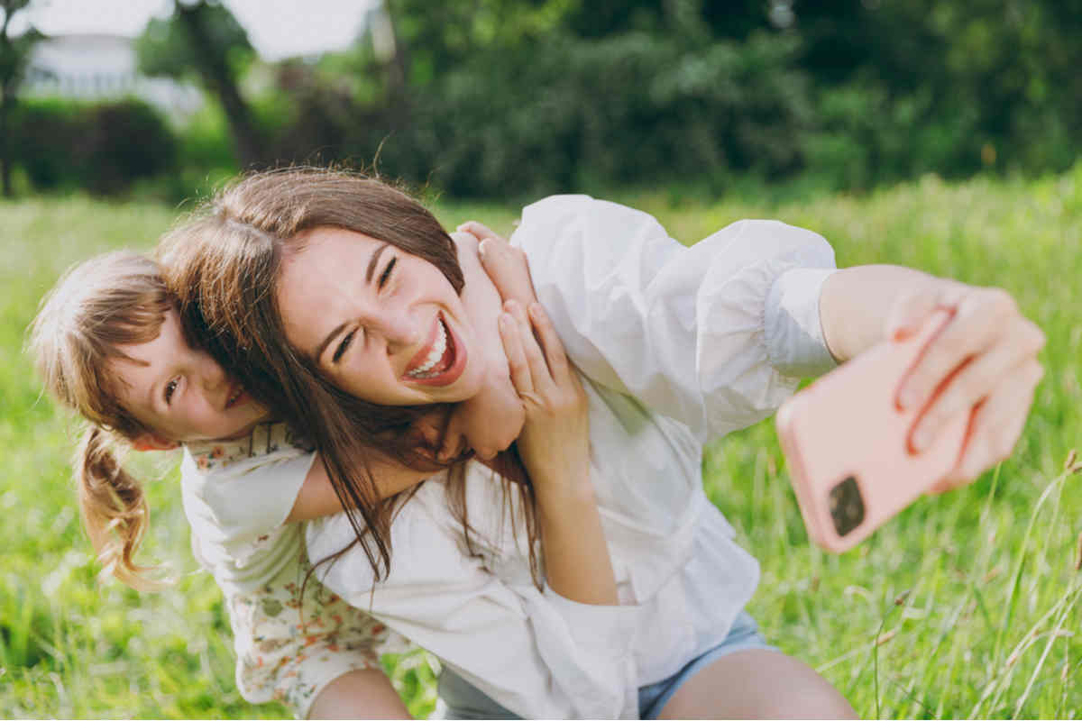 mamma e figlia sorridenti che si scattano una foto in un prato verde