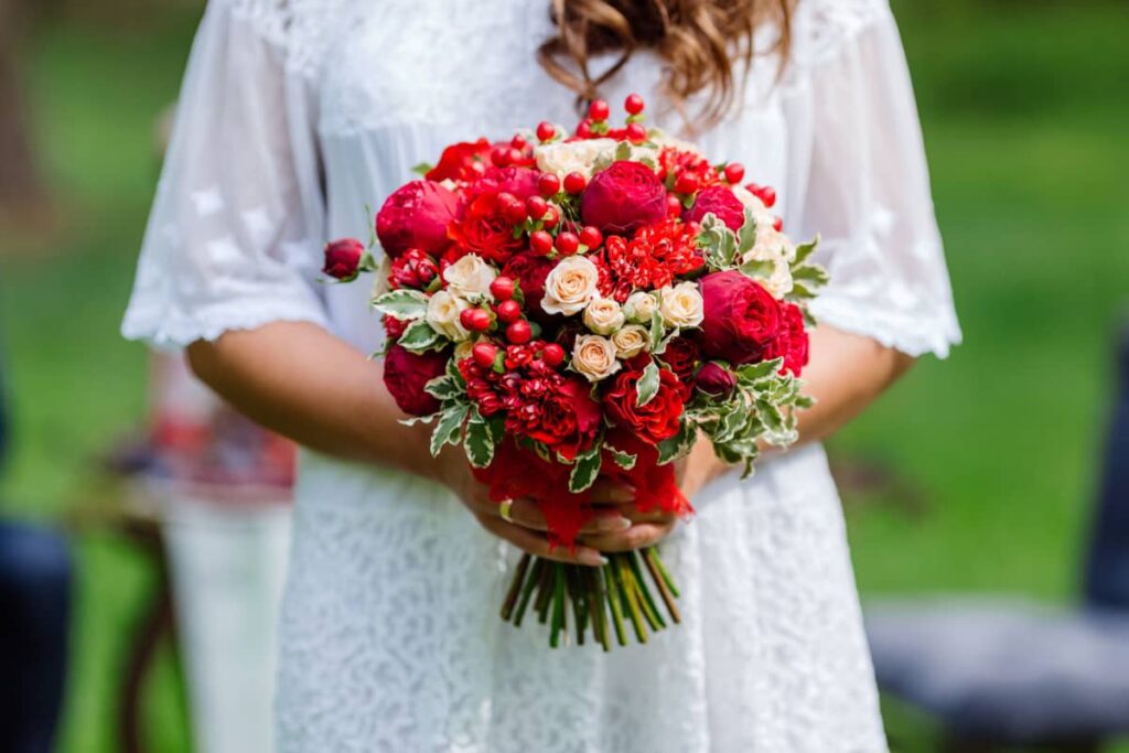 mani di sposa che tengono un bouquet con fiori rossi e bacche