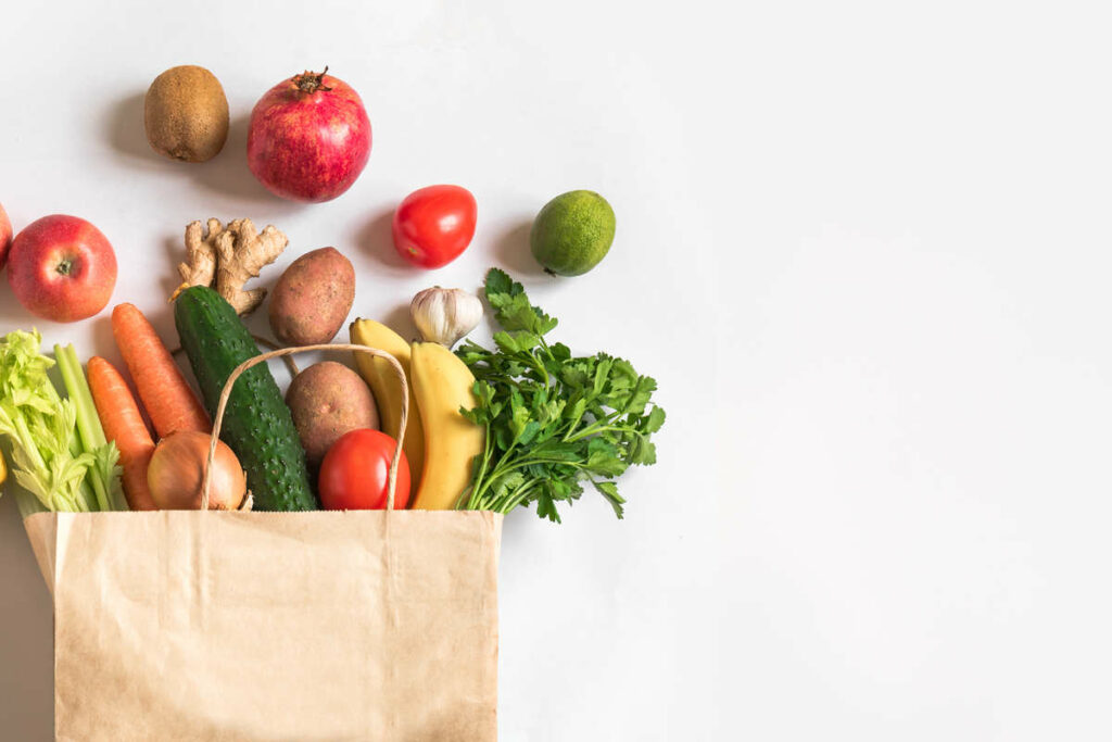 frutta e verdura di vario genere che fuoriescono da una busta di cartone 