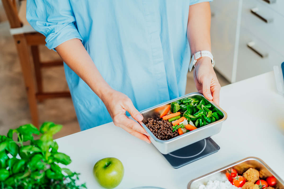 mani di ragazza che pesano il pasto completo di verdure e legumisulla bilancia