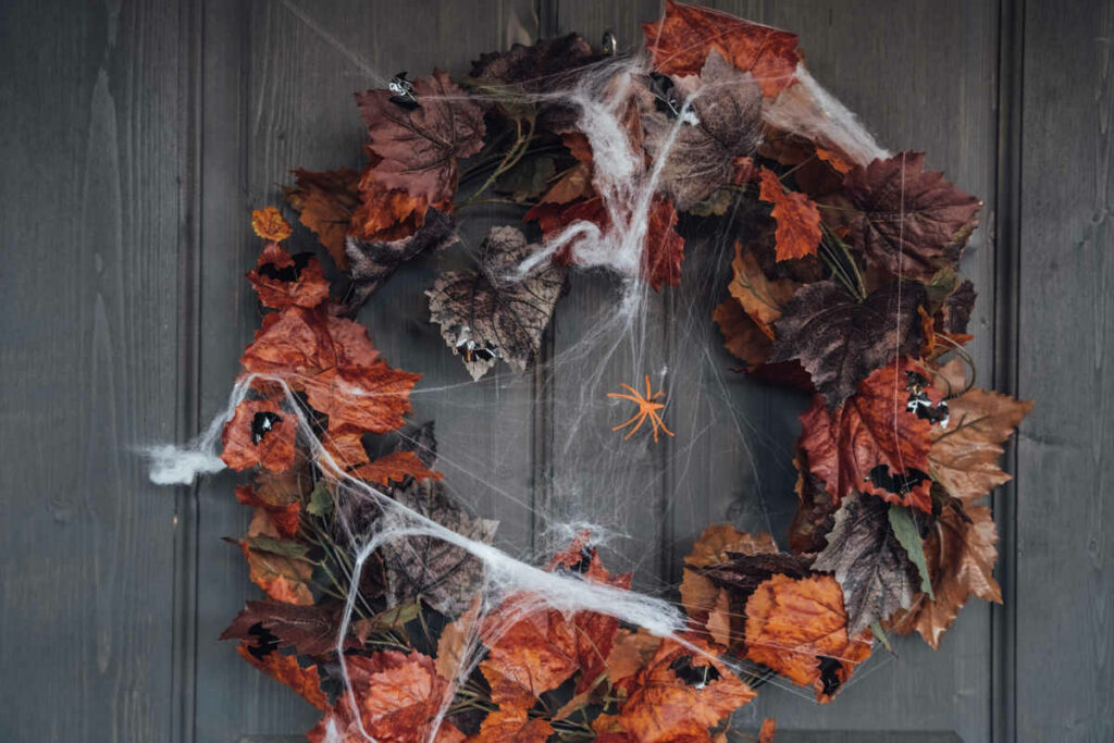 ghirlanda con fiori e foglie secchi di colore rosso e arancione, con ragnatele e ragnetti finti appesa ad una porta