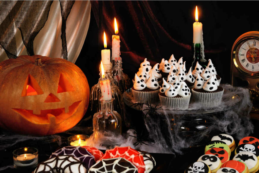 tavola con candele, zucca di halloween, muffin con meringhe fantasma e biscotti vari a tema halloween 