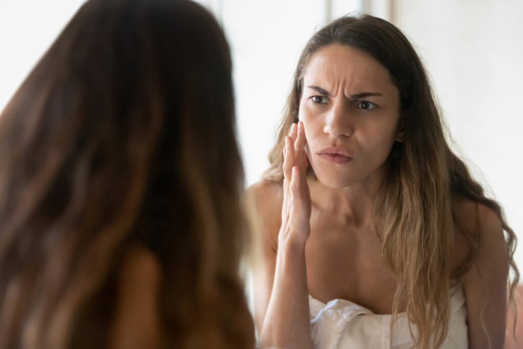 ragazza si guarda allo specchio, toccandosi il viso, con rughe glabellari