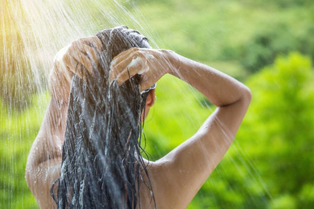 donna di schiena mentre si fa lo shampoo all'aperto, sfondo natura
