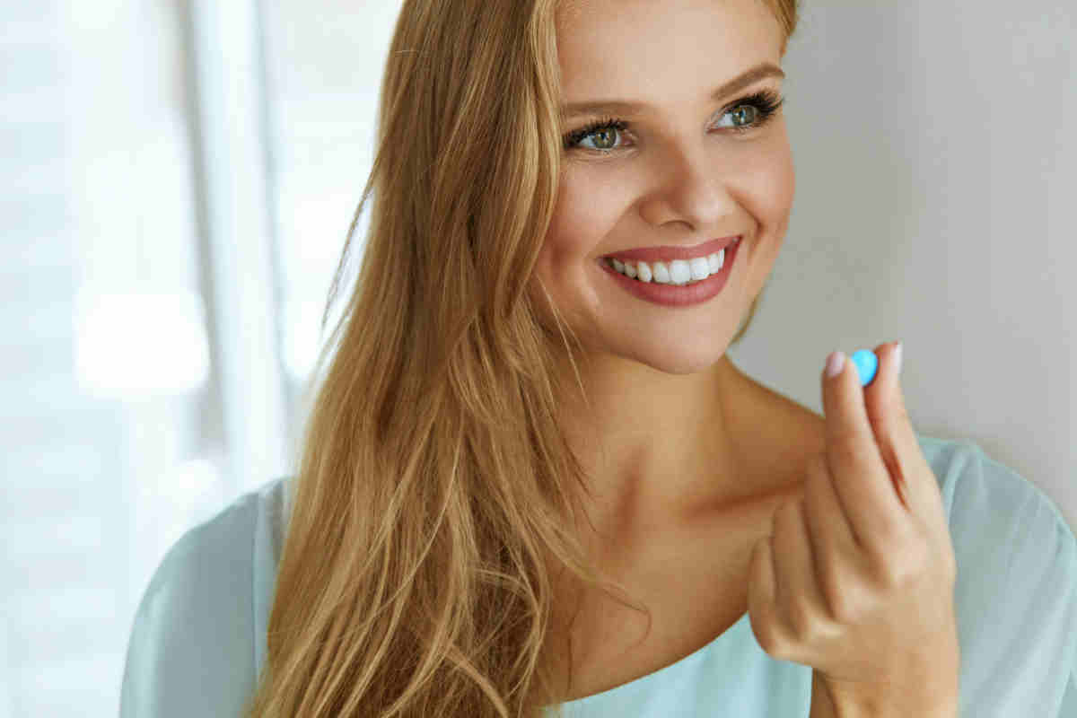 giovane ragazza bionda e sorridente che tiene una pillola in mano
