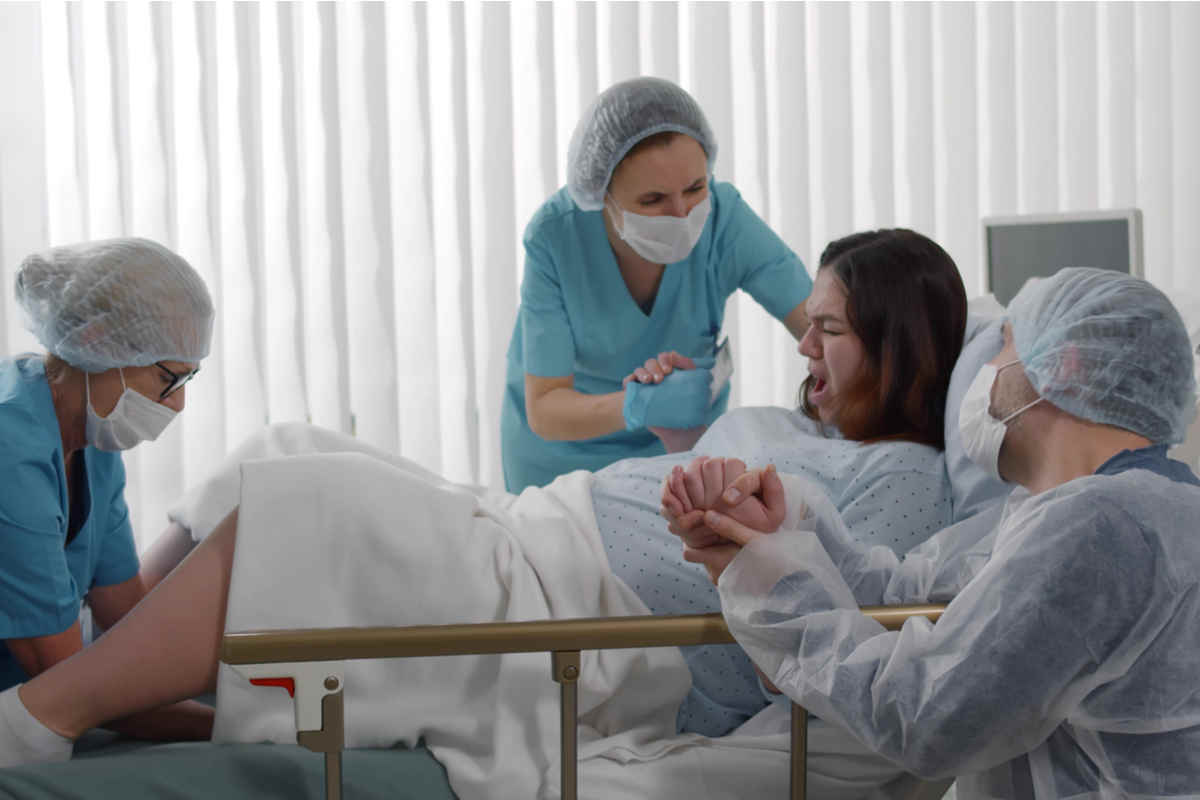 donna in preda ai dolori del parto su un letto di ospedale circondata da tre dottori