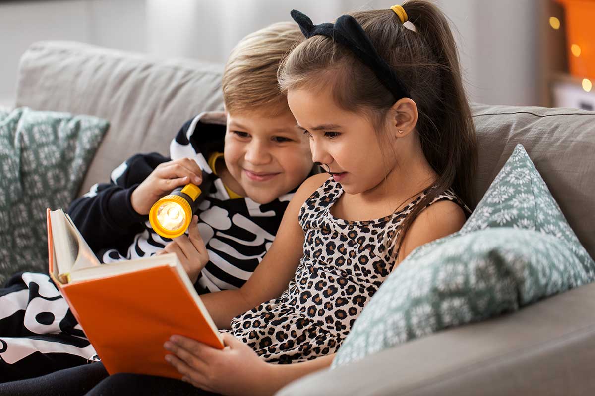 Bambini con vestiti di Carnevale mentre leggono un libro seduti sul divano