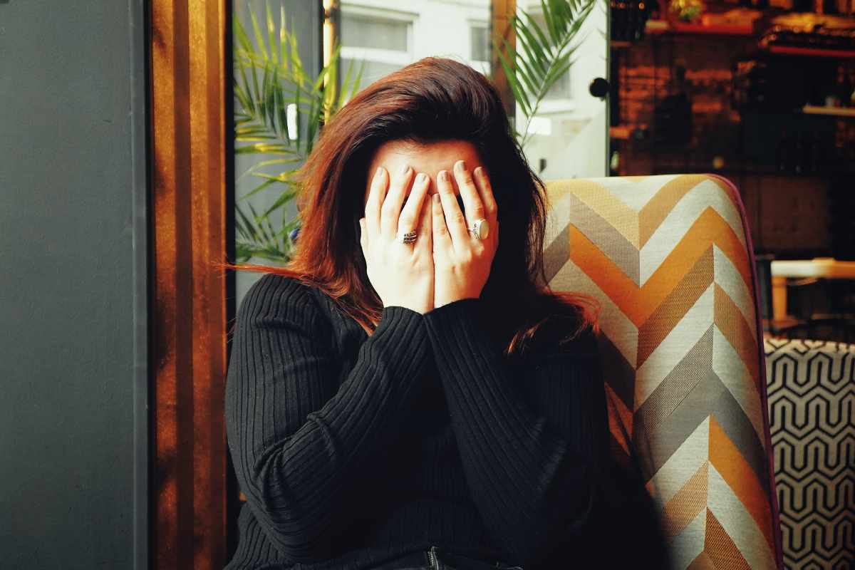 Donna con dolore cronico, seduta e con le mani in faccia