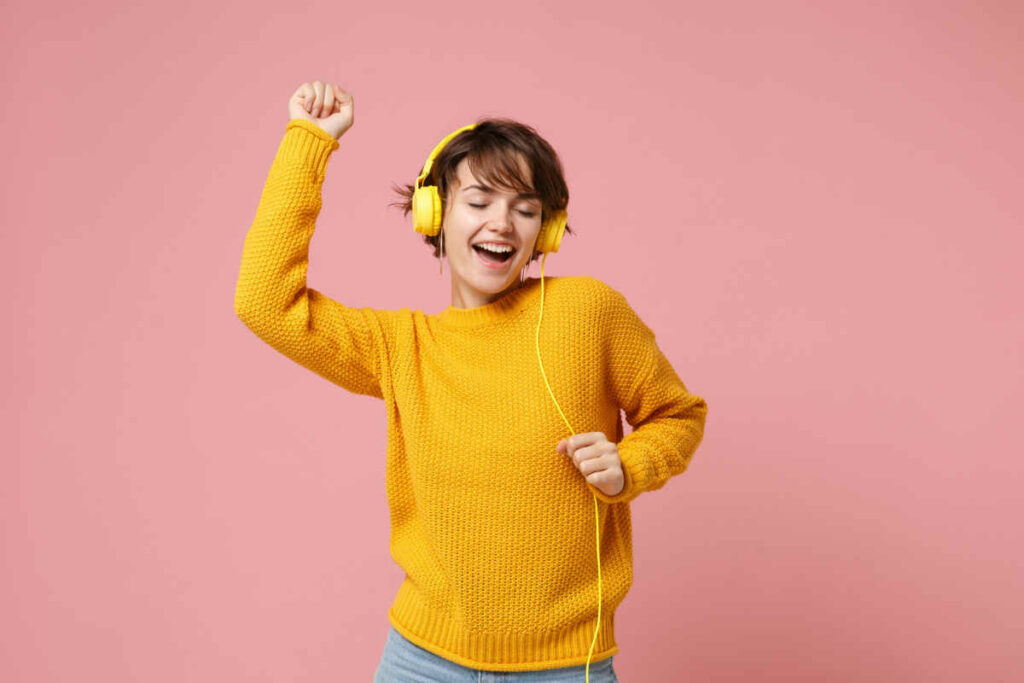 ragazza sorridente mentre ascolta musica, indossa un maglione giallo