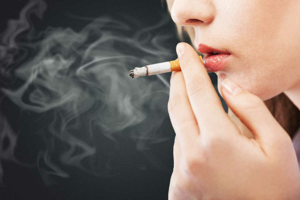 immagine con zoom su mani e labbra di ragazza che fuma una sigaretta