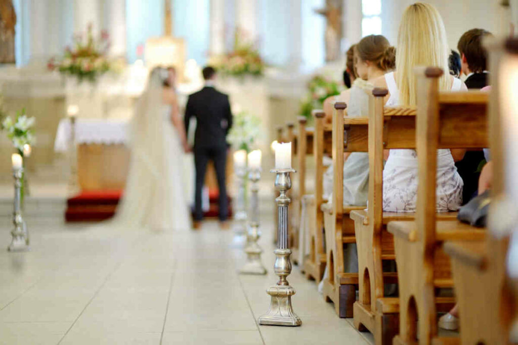 interno di una chiesa con candelabri, panche con persone sedute e in lontananza coppia di sposi