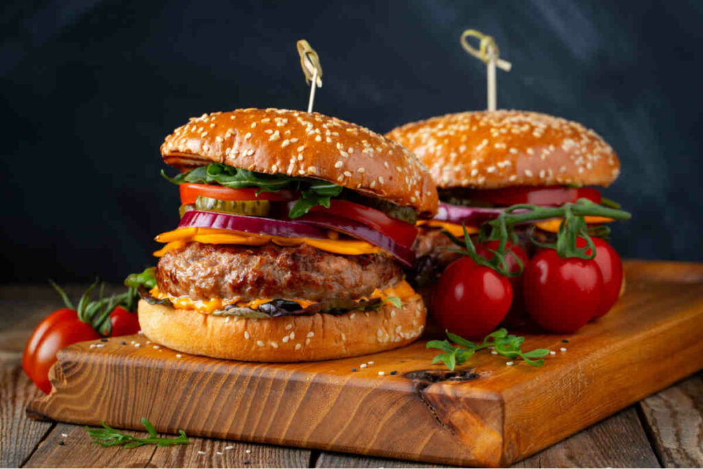 due panini con hamburger, pomodorini, salsa e cipolla, su una tavola di legno