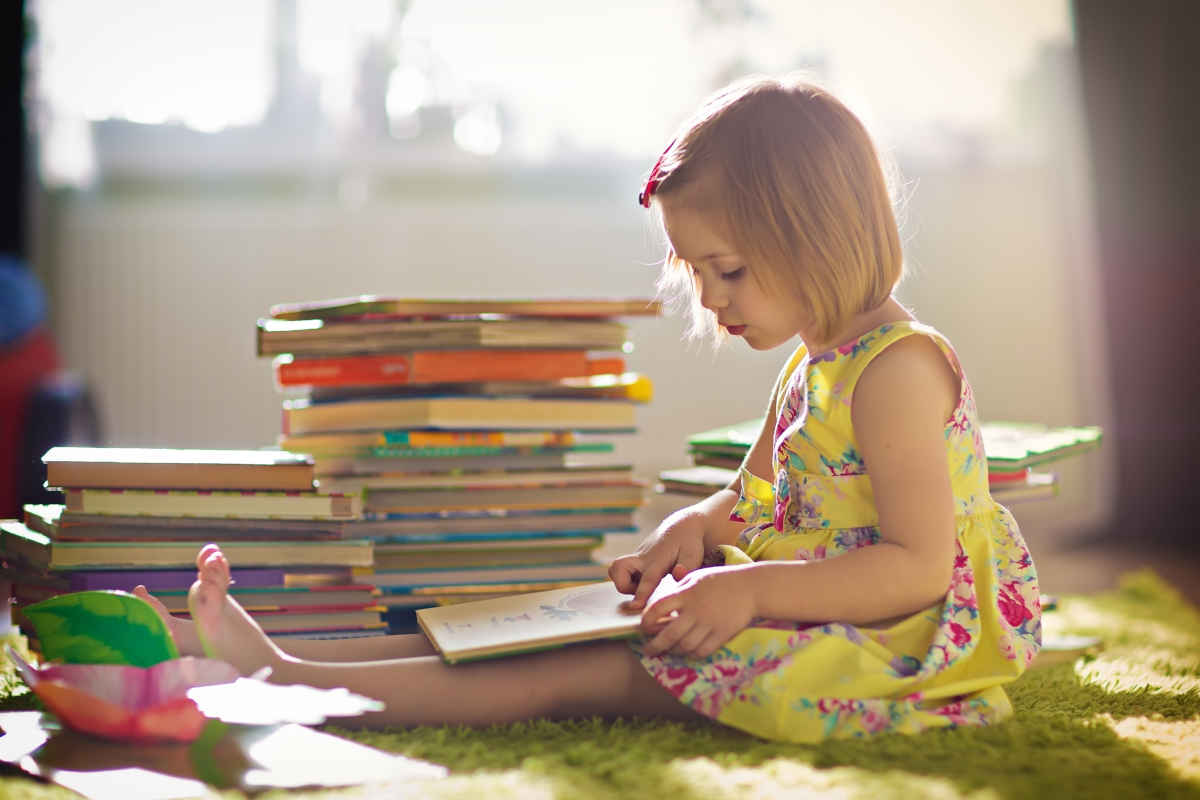 Bambina bionda con vestito giallo che legge un libro