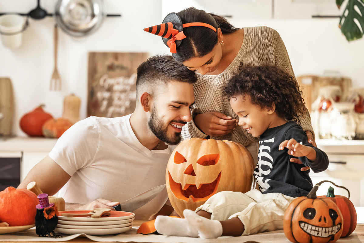 Coppia di genitori di famiglia multietnici allegri con il figlio che sorride mentre creano la zucca per Halloween in cucina