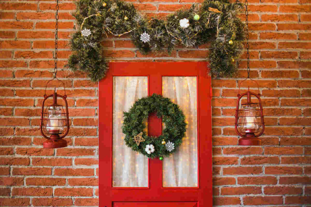 porta d'ingresso di colore rosso di un appartamento con ghirlanda appesa e decorazioni varie natalizie