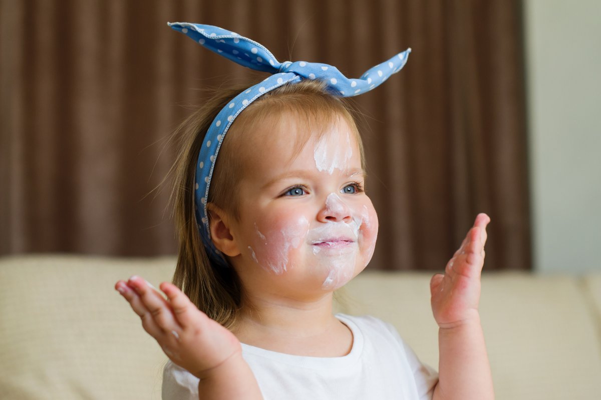 Bimba sorridente con una fascia in testa e della crema sul viso