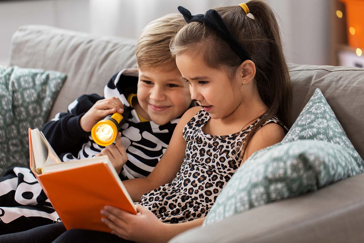 Bambini mascherati per Halloween che leggono un libro sul divano