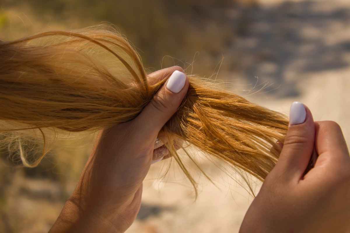 Ragazza che si tocca i capelli colorati sfibrati da sole e mare