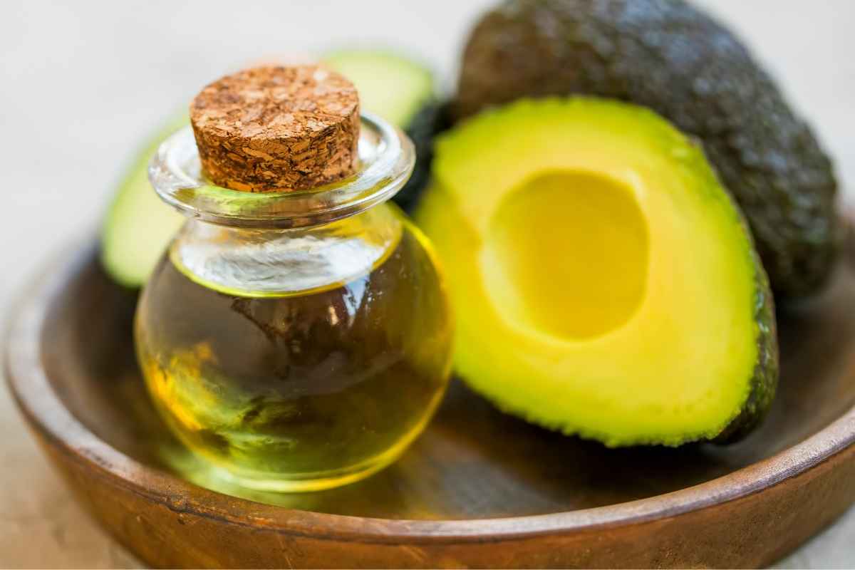 Vassoio in legno con sopra avocado e olio di oliva per fare una maschera nutriente per capelli