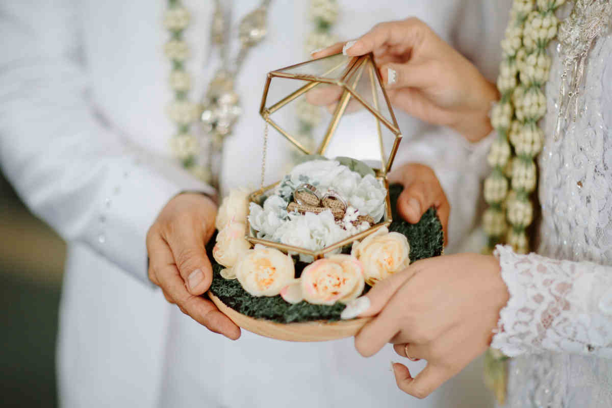 mani di ragazzo e ragazza che sorreggono un portafedi in legno con fiori