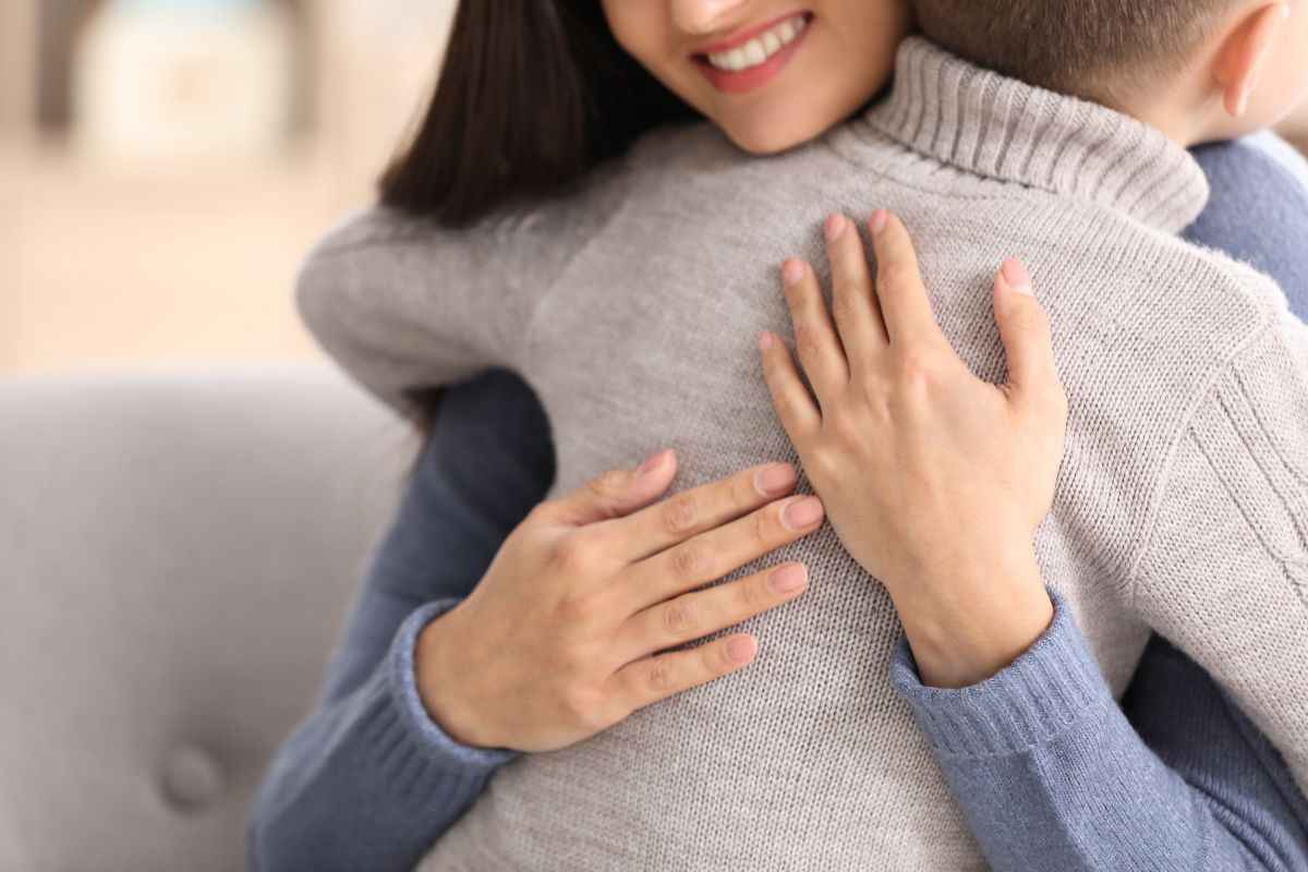 mamma che sorride e abbraccia il figlio che è di spalle