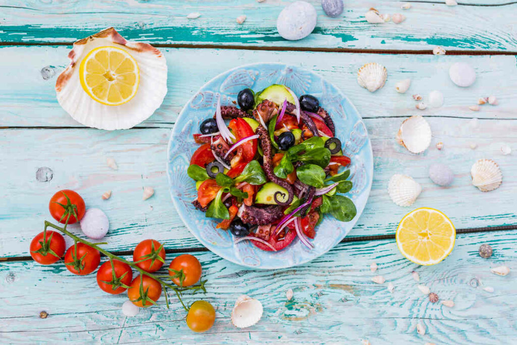 insalata con polpo, pomodorini, su tavolo in legno con pomodori, conchiglie e limone