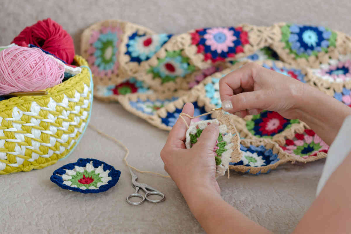 mani di ragazza che creano all'uncinetto tante piccole presine di molti colori