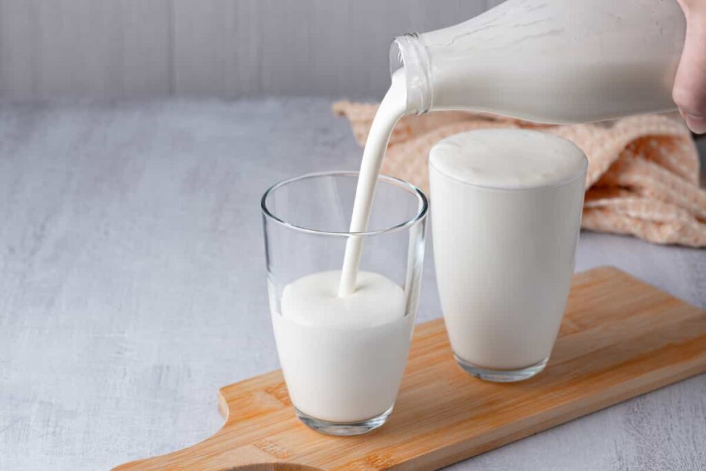 mani che versano il latte da una bottiglia in due bicchieri