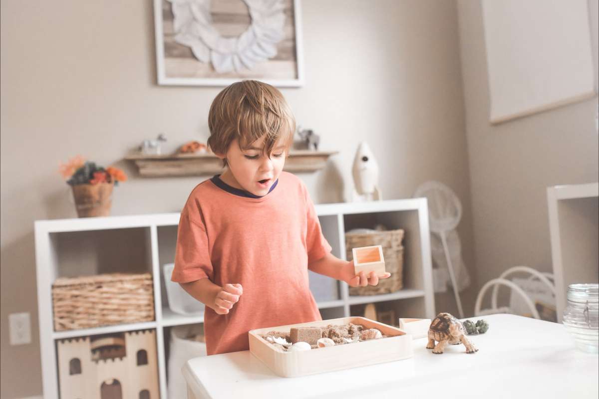 Un bambino in piedi su uno sgabello montessori che gioca