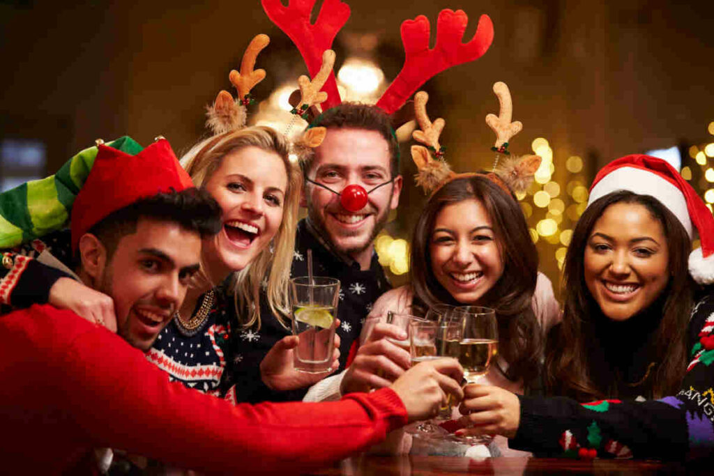 gruppo di ragazzi e ragazze sorridenti con cappelli di Natale e corna di renne, mentre brindano