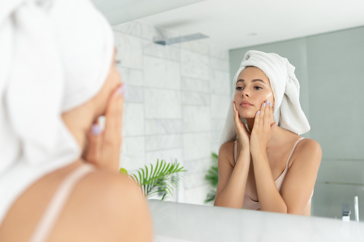 ragazza allo specchio, con asciugamano in testa, che applica la crema sul viso