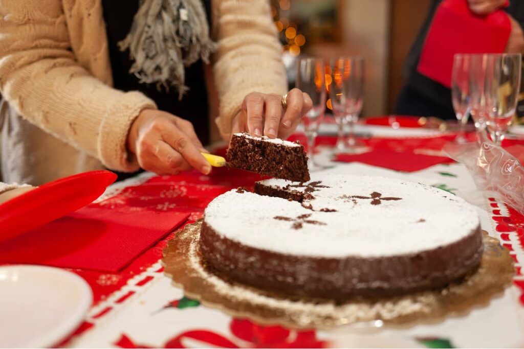 tavola di Natale con signora che taglia torta caprese al cioccolato