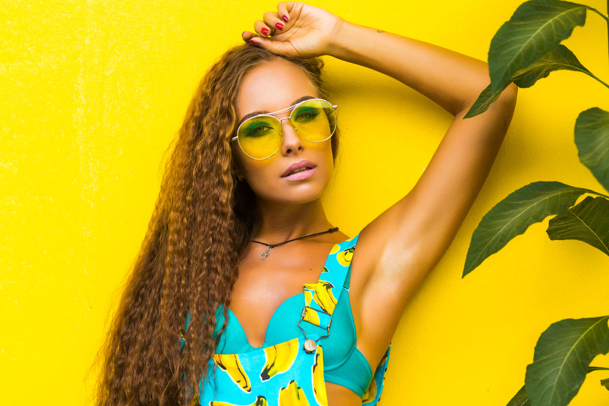 ragazza con occhiali da sole gialli e piante tropicali