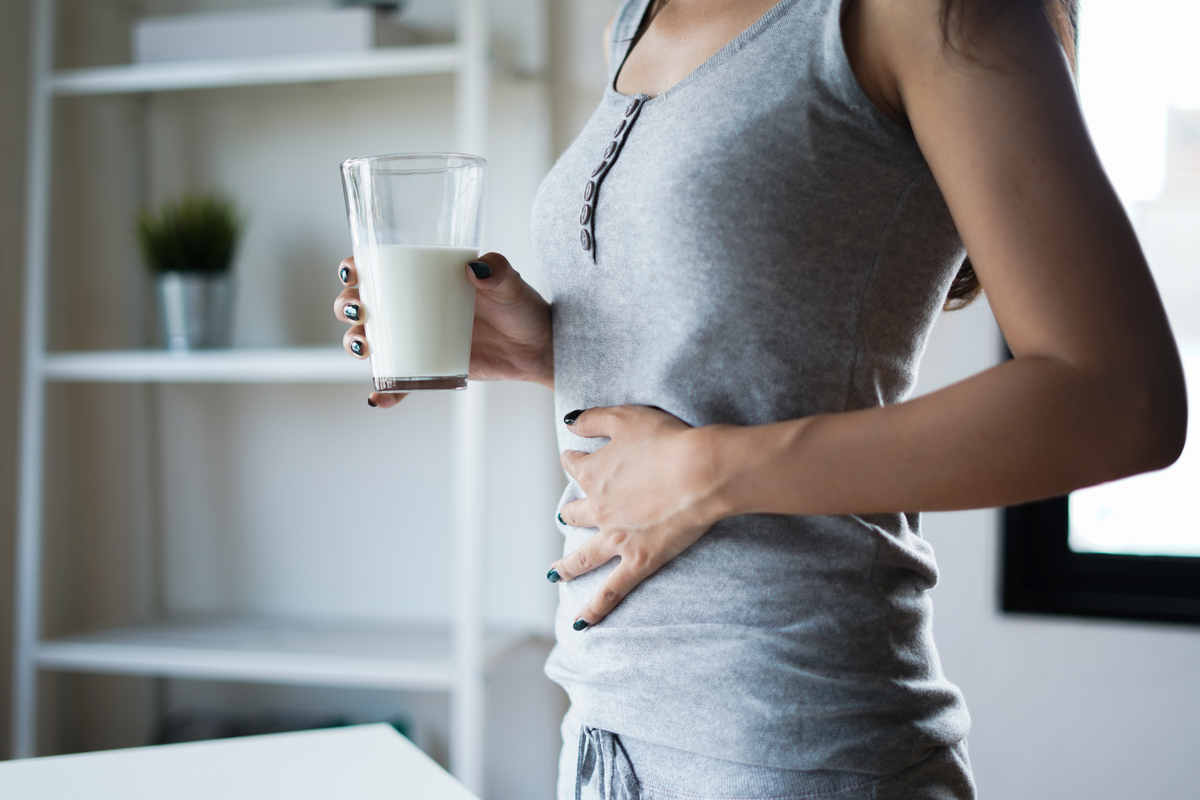 ragazza che con una mano si tocca la pancia e con l'altra tiene un bicchiere di latte