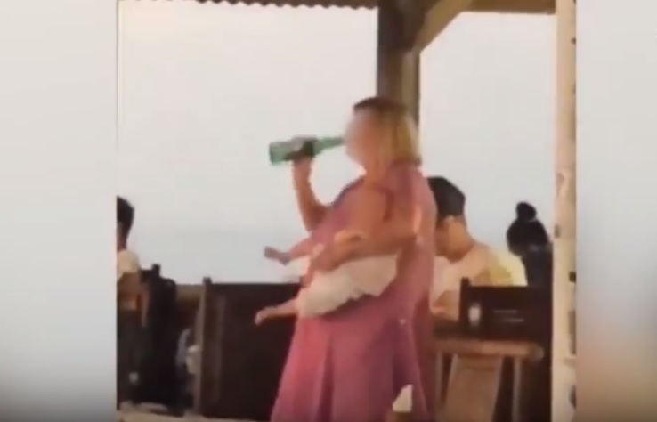 Mamma tiene in braccio un neonato in lacrime mentre si scola una birra in un solo sorso: il video shock