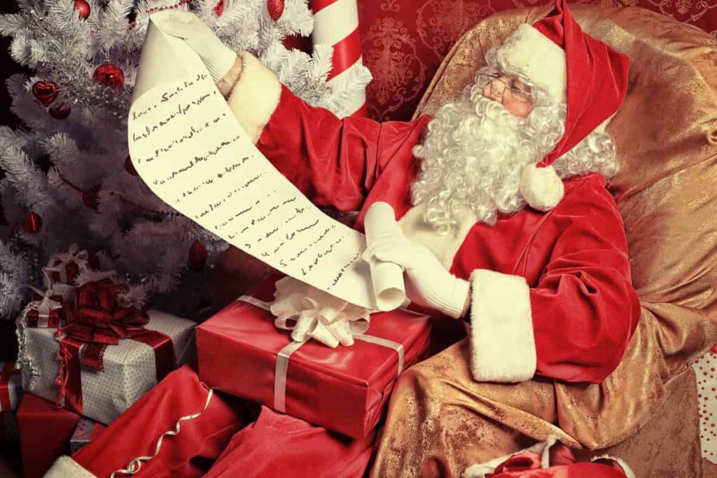 babbo natale vestito di rosso con barba bianca che legge un papiro circondato da regali di natale
