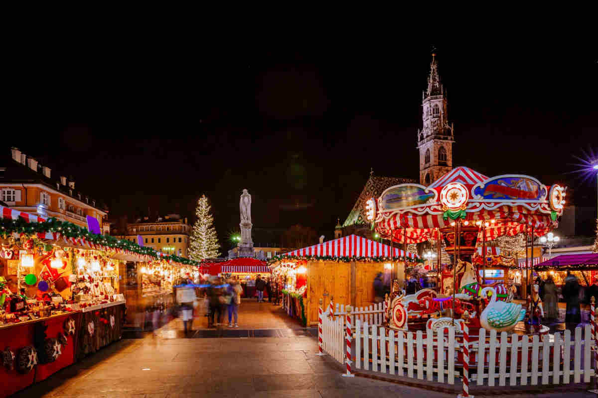 piazza illuminata dalle luci di Natale, con giostre e casette di legno per i mercatini tipici