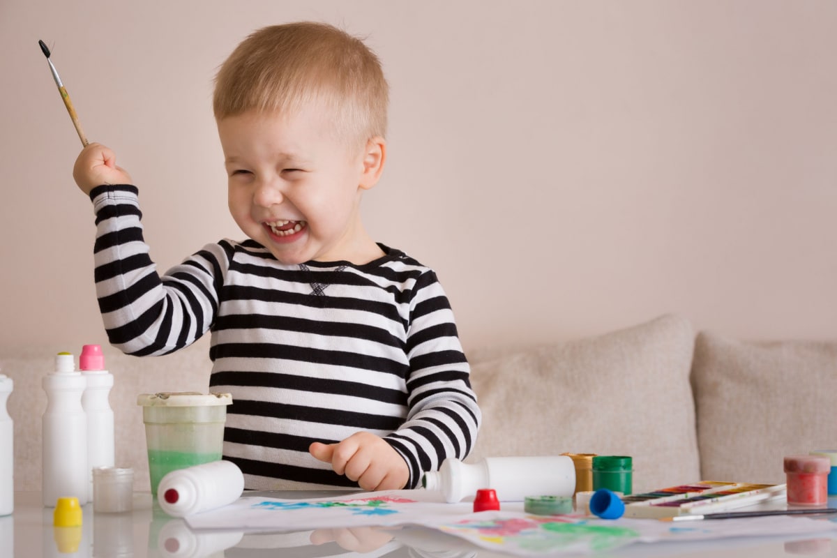 bambino sorridente con maglia a righe che colora con i pennelli