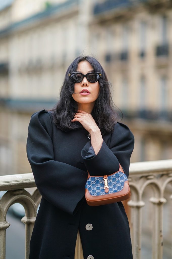 La fashion blogger Xiayan indossa occhiali da sole di Bottega Veneta, un lungo cappotto di lana nera con spalline di Lovechild, una borsa Gucci stampata con monogramma blu e marrone realizzata in denim e pelle, il 31 gennaio 2021 a Parigi, Francia.