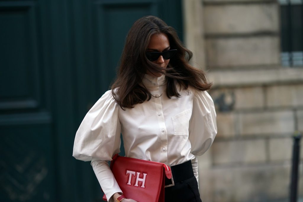 Therese Hellström indossa occhiali da sole, una camicia bianca con spalle / maniche a sbuffo, una borsa di pelle rossa, pantaloni neri, il 28 novembre 2020 a Parigi, Francia