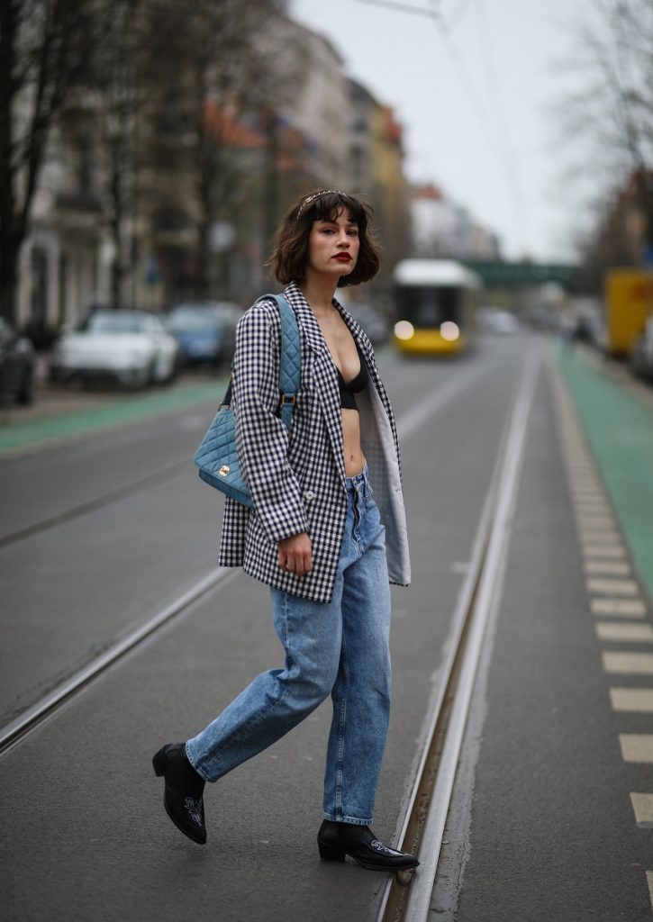 Lea Naumann indossa una borsa e una fascia di jeans Chanel, jeans blu Calvin Klein, top corto nero degli Armed Angels, blazer vintage e stivali Gestuz neri il 1 ° aprile 2021 a Berlino, Germania