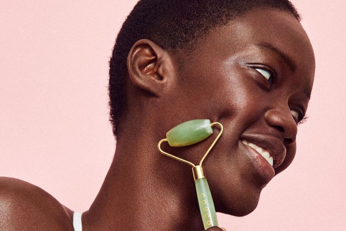 ragazza sorridente mentre massaggia il viso con jade roller, sfondo rosa
